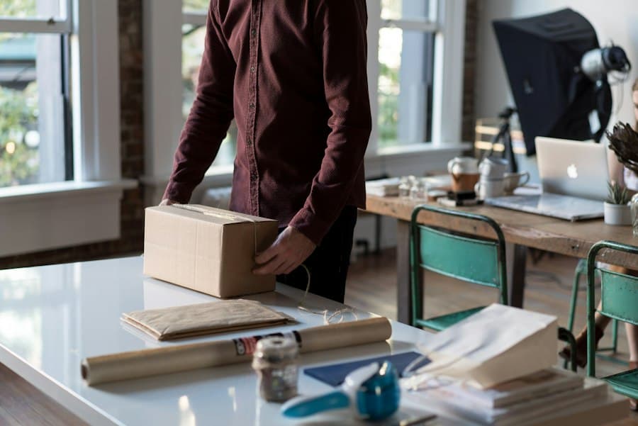 Un homme ferme un carton sur une table d'atelier, un ordinateur portable ouvert au fond
